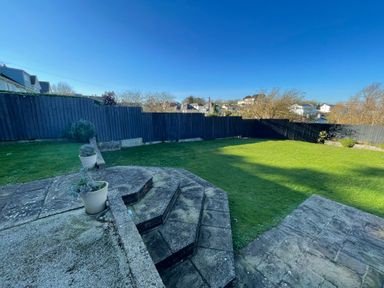 A backyard with a lawn stone steps and potted plants with a black wooden fence in the background at Raleigh House in Salcombe