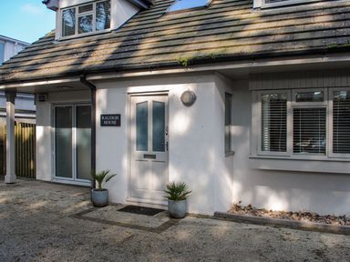 The outside entrance of a house with a door labeled Raleigh House and two plants in pots at Raleigh House in Salcombe