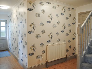 A hallway with fish patterned wallpaper wooden floor a radiator a staircase and a door at Raleigh House in Salcombe