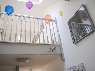 A stairway with white railing and colorful balloons attached to the railing and ceiling at Raleigh House in Salcombe