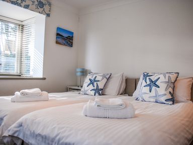 A bedroom with two single beds white linens starfish patterned pillows a window and a bedside table with a lamp at Raleigh House in Salcombe