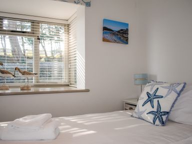 A bedroom with a bed that has a starfish pillow and folded towels near a window with bird decorations on the sill at Raleigh House in Salcombe