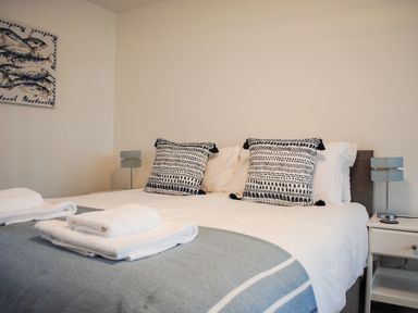 A bedroom with a bed with patterned pillows folded towels bedside tables and lamps at Raleigh House in Salcombe