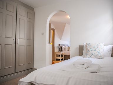 A bedroom with a bed with white linens and towels with an arch doorway leading to another room with a bed and a bedside table at Raleigh House in Salcombe