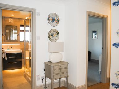 A small wooden table with a lamp between a bathroom and a room with a framed picture on the wall at Raleigh House in Salcombe