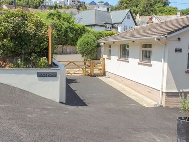 A driveway leading to a white building with windows and a wooden gate surrounded by greenery at Rock Point Salcombe