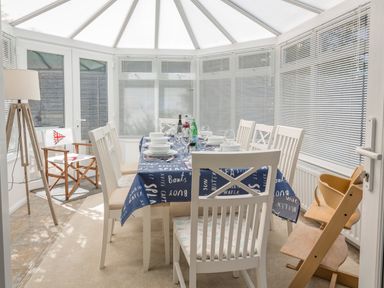 A dining area in a conservatory with a table set for eight and a high chair at Rock Point in Salcombe