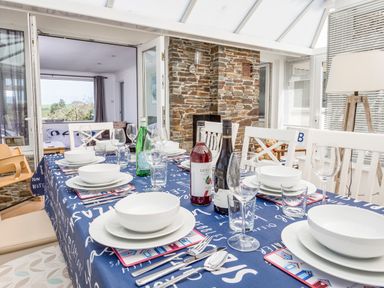 A dining table with white plates glasses bottles and cutlery in a conservatory with stone wall at Rock Point in Salcombe