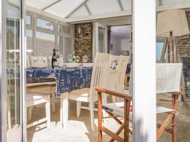 A dining area with a table covered by a blue tablecloth surrounded by white chairs and a wooden chair with a fabric seat at Rock Point in Salcombe