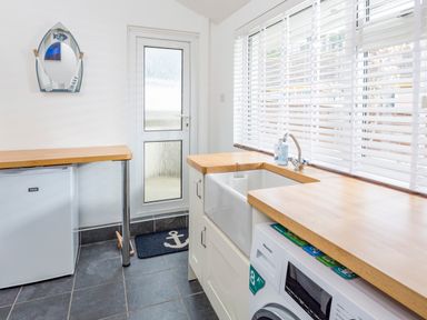 A utility room with a washing machine a sink a small fridge and a window with blinds at Rock Point in Salcombe