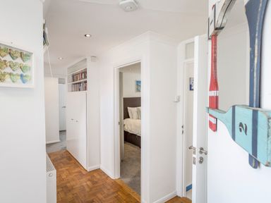 A hallway with wooden flooring bookshelves and two open doors showing a bedroom and another room at Rock Point Salcombe
