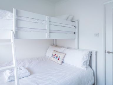 A white bunk bed with a double bed on the bottom and a single bed on top with white bedding and a decorative pillow in a bedroom at Rock Point in Salcombe