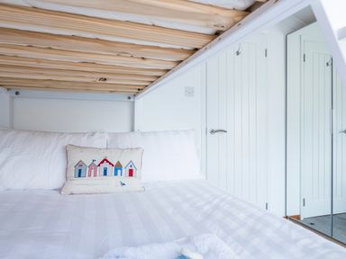A bunk bed with a white bedspread and a decorative pillow with beach huts in a white room with doors and a mirror at Rock Point Salcombe