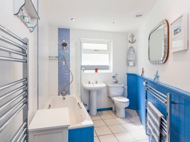A bathroom with a bathtub shower toilet and sink with blue paneling and tile at Rock Point in Salcombe