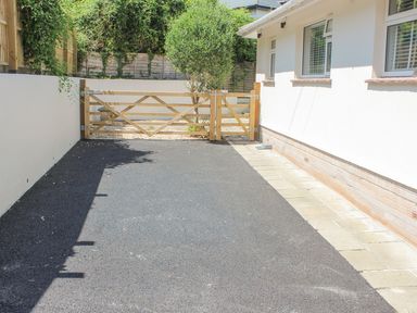 A black asphalt driveway leading to a wooden gate next to a white house with windows at Rock Point in Salcombe