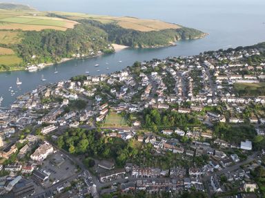 An aerial view of a town with houses trees roads a river with boats and fields in the background at Rock Point in Salcombe
