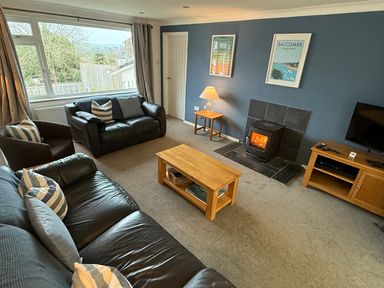 A living room with black leather sofas wooden coffee tables a lit fireplace and a television at Rock Point in Salcombe