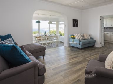 A living room with sofas and a dining area with a table and chairs by a window showing an outdoor view at Seaspray Bigbury-on-Sea