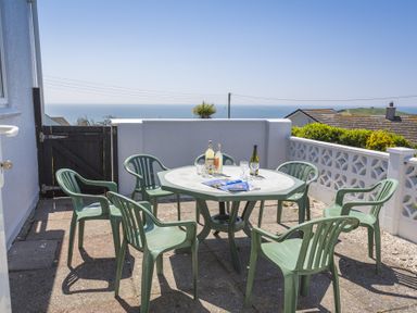 A patio area with a round table and six chairs overlooking the sea at Seaspray Bigbury-on-Sea