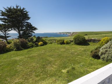 A grassy garden with shrubs and trees overlooking a coastal landscape with cliffs and the sea at Seaspray Bigbury-on-Sea