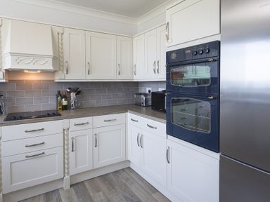 A kitchen with white cabinets wooden countertops a black double oven a stainless steel fridge and a gray tiled backsplash at Seaspray Bigbury-on-Sea