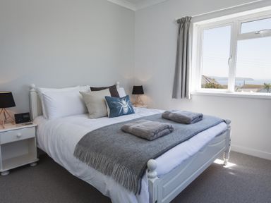 A bedroom with a double bed gray throw on the bed bedside tables with black lamps and a window with curtains at Seaspray Bigbury-on-Sea