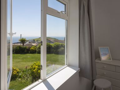A window open to a garden with bushes and a view of houses and the sea at Seaspray Bigbury-on-Sea