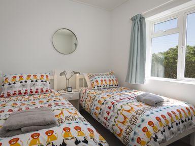 A bedroom with two single beds with animal print bedding and a window with curtain at Seaspray Bigbury-on-Sea in Bigbury-on-Sea