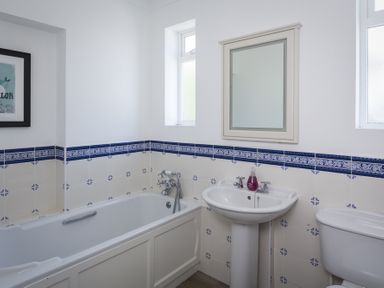 A bathroom with a bathtub sink toilet mirror and decorative blue and white tiles at Seaspray in Bigbury-on-Sea