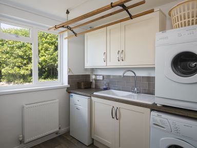 A utility room with a window a sink cabinets a radiator a washing machine and a dryer at Seaspray Bigbury-on-Sea