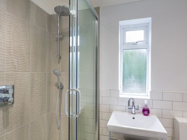 A bathroom with a glass shower enclosure a showerhead a rectangular sink with a faucet and a window above the sink at Seaspray Bigbury-on-Sea