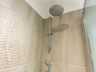 A shower area with wall tiles and two shower heads at Seaspray Bigbury-on-Sea in Bigbury-on-Sea