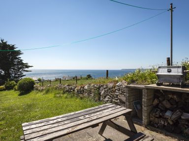 An outdoor area with a wooden picnic table a barbecue and a view of the sea at Seaspray Bigbury-on-Sea