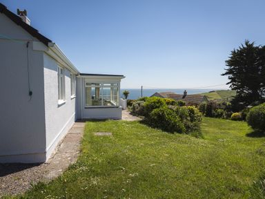 A side view of a white house with a garden and sea view at Seaspray Bigbury on Sea