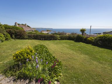 A garden with flower beds and grass overlooking houses and the sea at Seaspray Bigbury-on-Sea