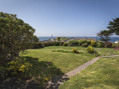 A garden with grass, shrubs, a paved pathway, and a view of the sea at Seaspray (Bigbury-on-Sea) in Bigbury-on-Sea