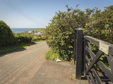 A rural road with bushes and a wooden gate overlooking the sea at Seaspray Bigbury-on-Sea