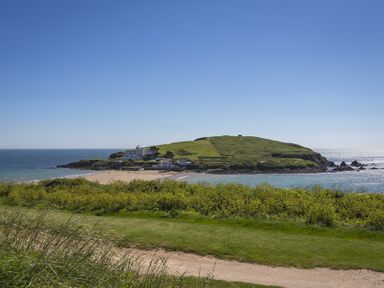 A grassy path overlooking a beach and a small island with buildings surrounded by water at Seaspray Bigbury-on-Sea
