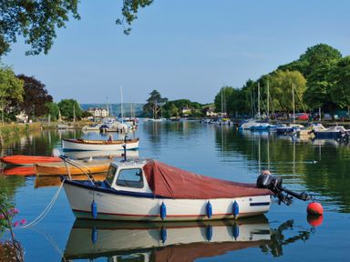 A river with boats moored along the banks and trees on either side at Seaspray Bigbury-on-Sea