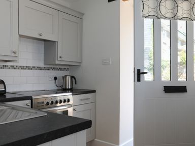 A kitchen corner with a stove kettle toaster and a door with glass panels at Stable End Cottage in Malborough
