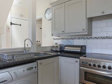 A kitchen corner with a sink dish rack washing machine toaster bread box and stove at Stable End Cottage in Malborough