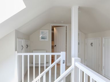 A hallway with white railings a partially open door built-in cupboards and a framed picture at Stable End Cottage in Malborough