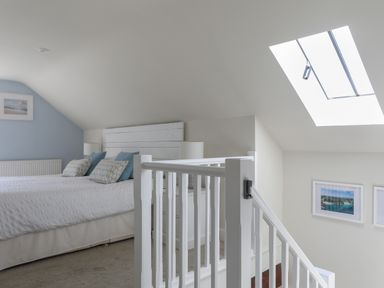 A bedroom with bed and pillows next to a staircase and skylight at Stable End Cottage in Malborough