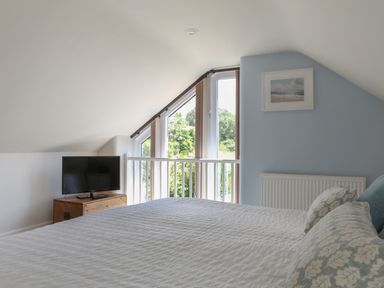 A bedroom with a bed and pillows a television on a wooden chest and a window with vertical blinds at Stable End Cottage in Malborough