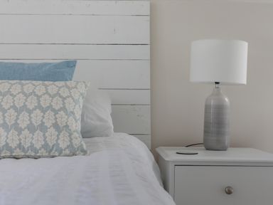 A bed with pillows and a white nightstand with a lamp at Stable End Cottage in Malborough
