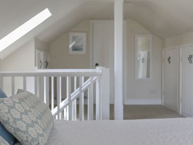 A bedroom with a bed and pillows near a stair railing with doors and a mirror on the walls at Stable End Cottage in Malborough