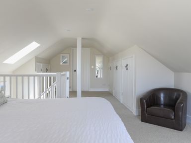 A bedroom attic space with a bed, staircase, small cupboards, a wall mirror and a leather armchair at Stable End Cottage in Malborough