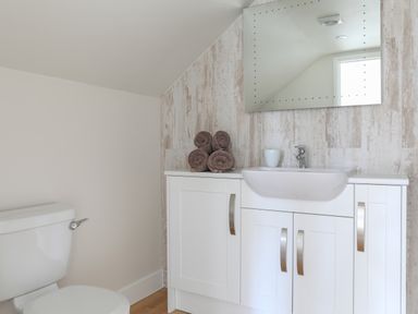 A bathroom with a toilet a white sink cabinet with rolled towels and a mirror at Stable End Cottage in Malborough