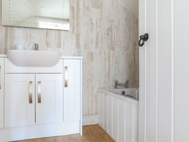 A bathroom with a white sink cabinet a bathtub and a mirror at Stable End Cottage in Malborough