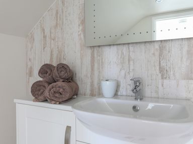 A bathroom sink with a faucet brown rolled towels and a white container on a countertop at Stable End Cottage in Malborough